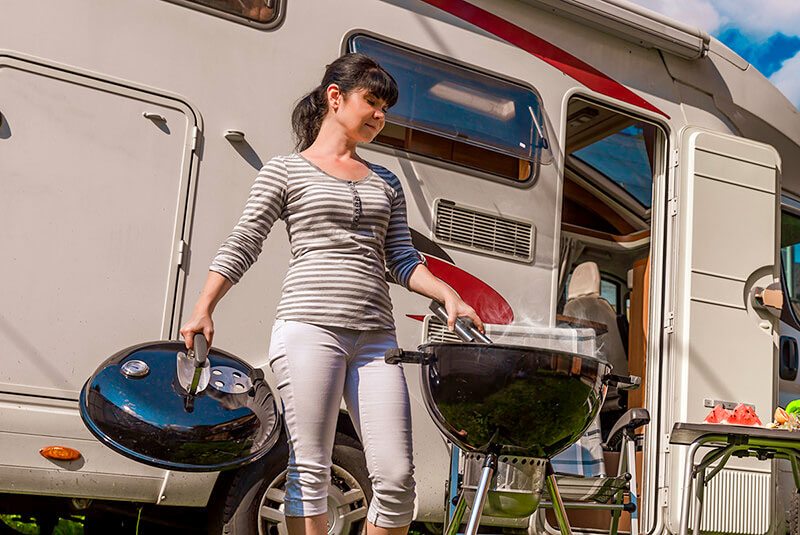 Woman cooks breakfast on Weber grill near RV