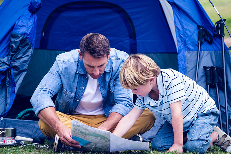 Father and young son by blue tent look at map
